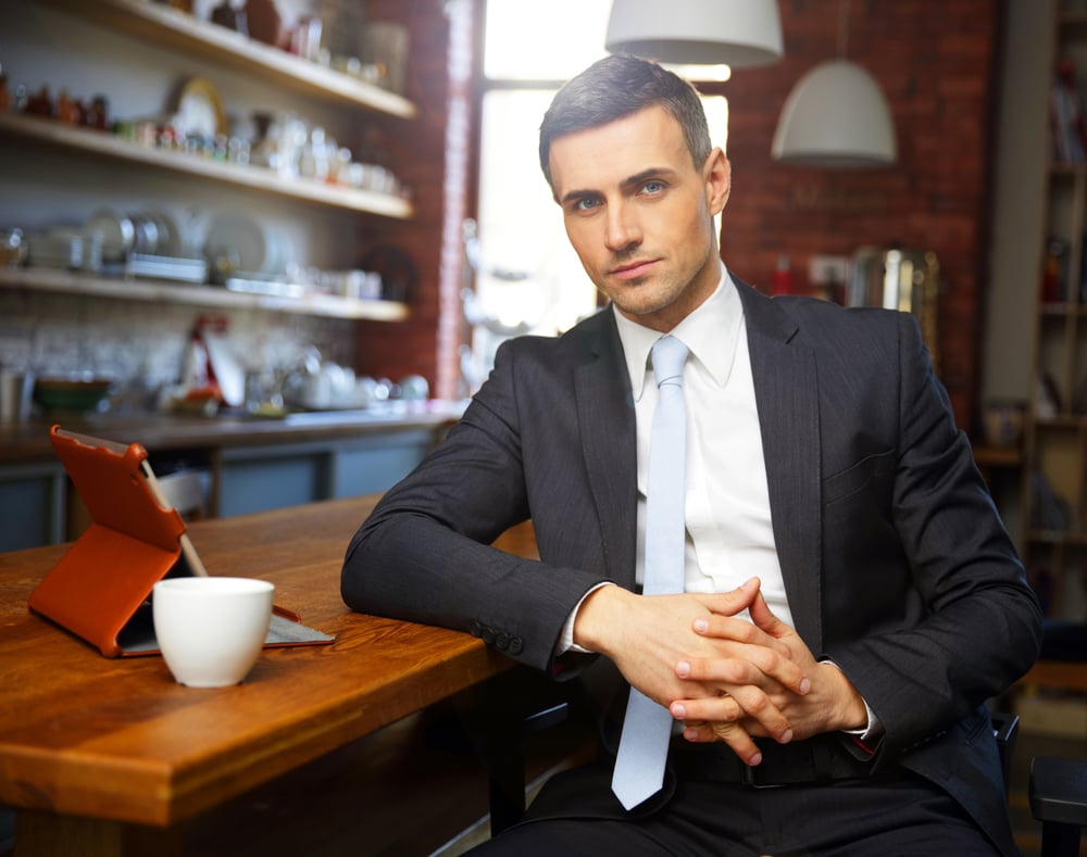 Confident businessman in formal cloths drinking coffee and reading news in the kitchen