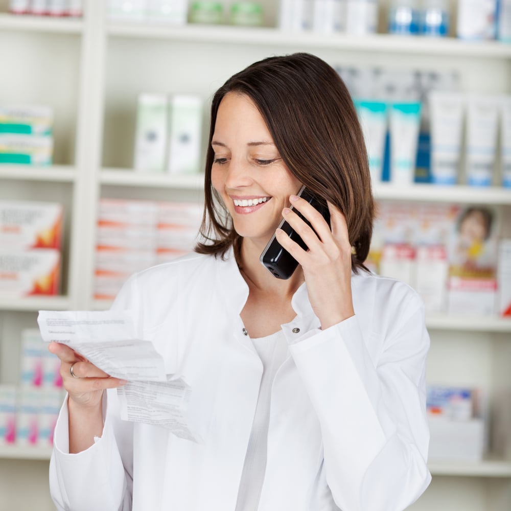 Mid adult female pharmacist holding prescription paper while using cordless phone in pharmacy-1